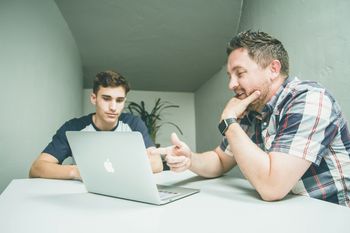 A person talking and mentoring another person on table with laptop on top of it